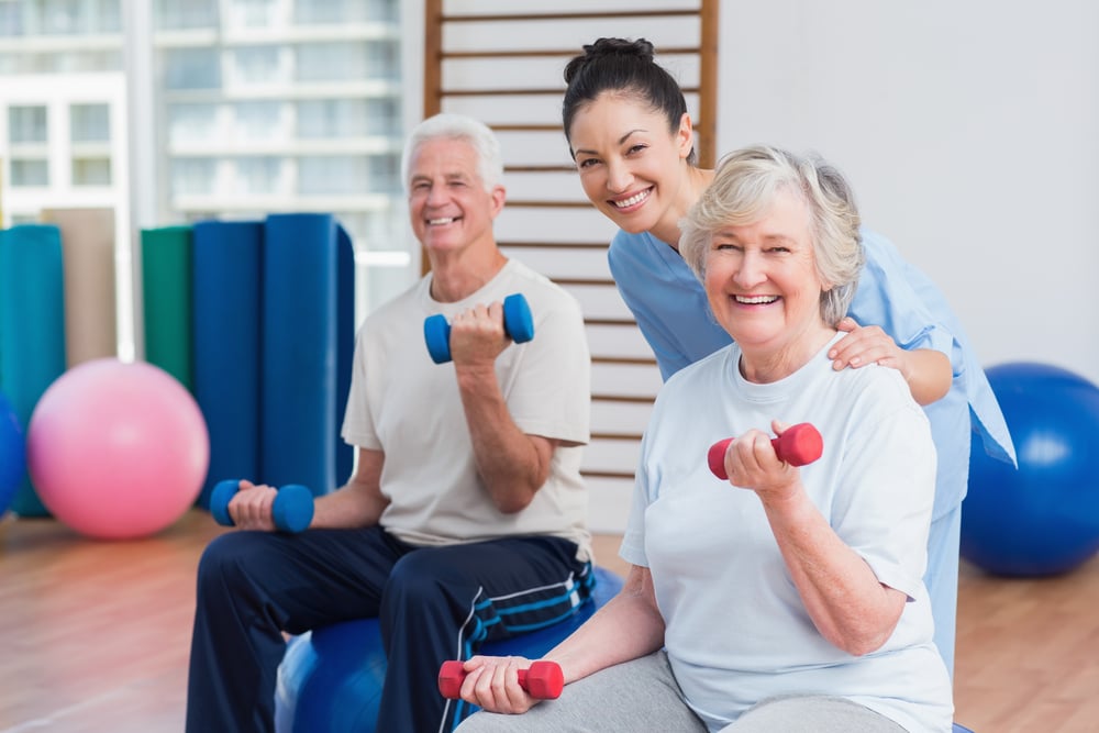 Portrait of happy female instructor with senior couple in gym-1